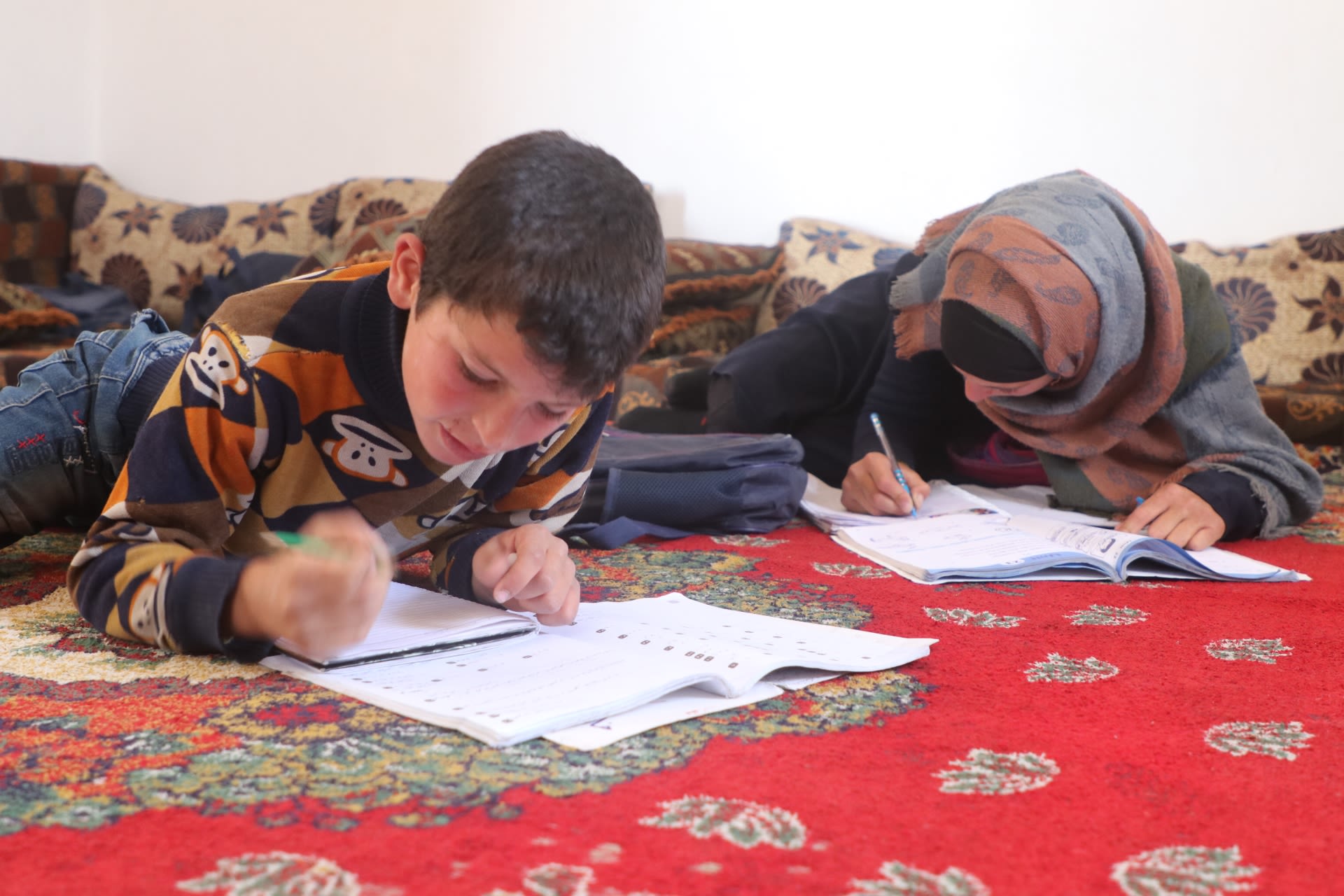 Kareem*, 9, les on a red carpet with pen in hand to complete his school work